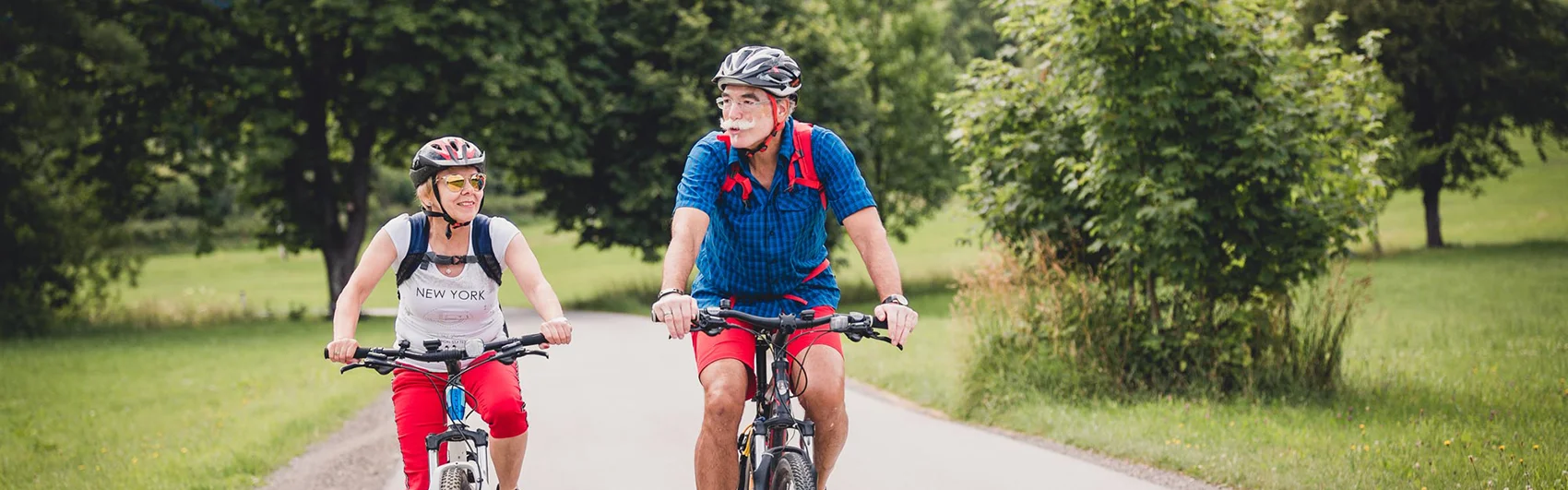 Radfahrer-Pärchen unterwegs am Mürztal-Radweg - Im Hintergrund Bäume und Wiesen.